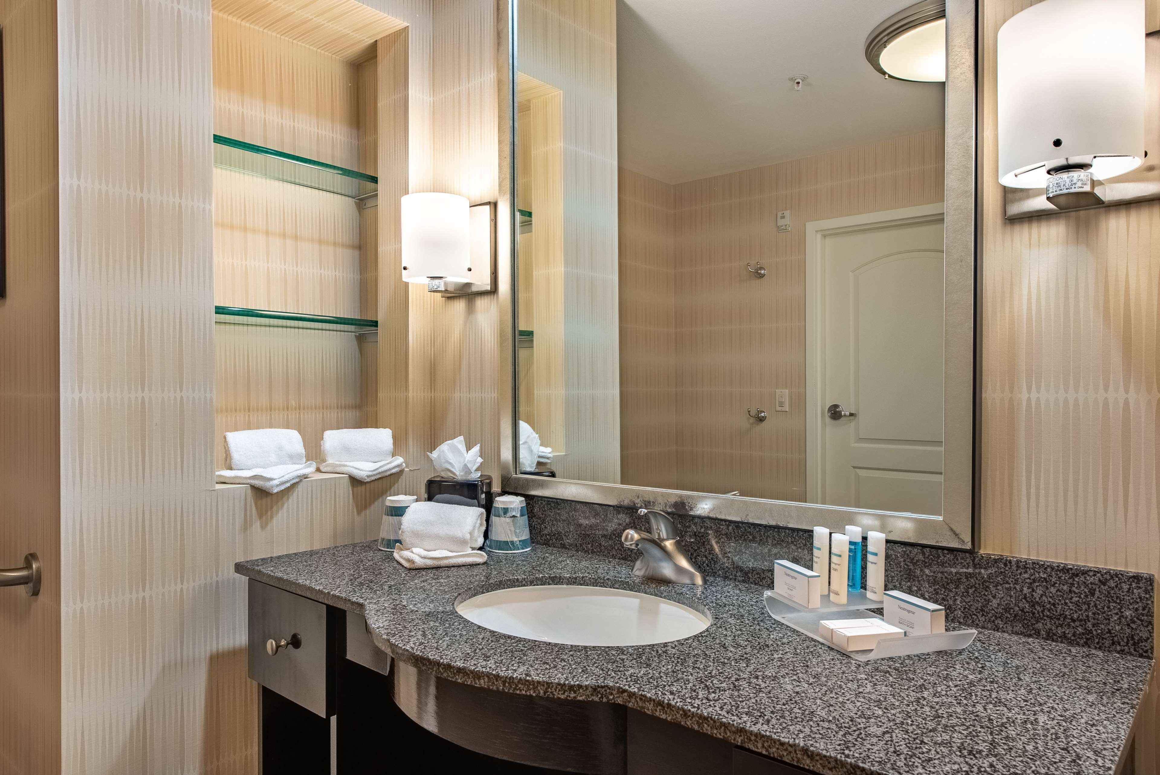 A modern bathroom with a granite countertop, a white sink, a large mirror, and a glass shower enclosure.