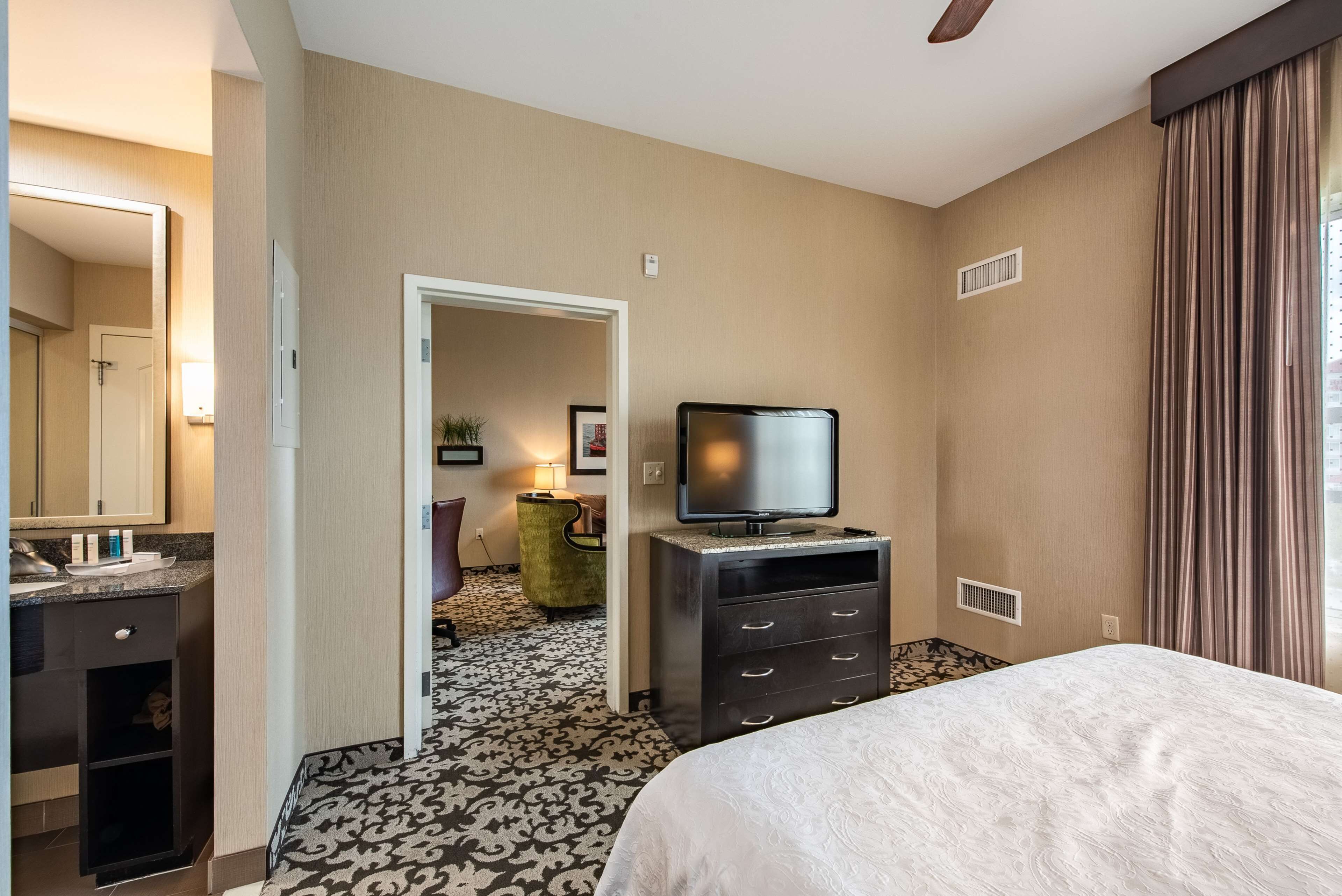 A hotel room with a bed, a television on a dresser, a mirror, and a door leading to another room.