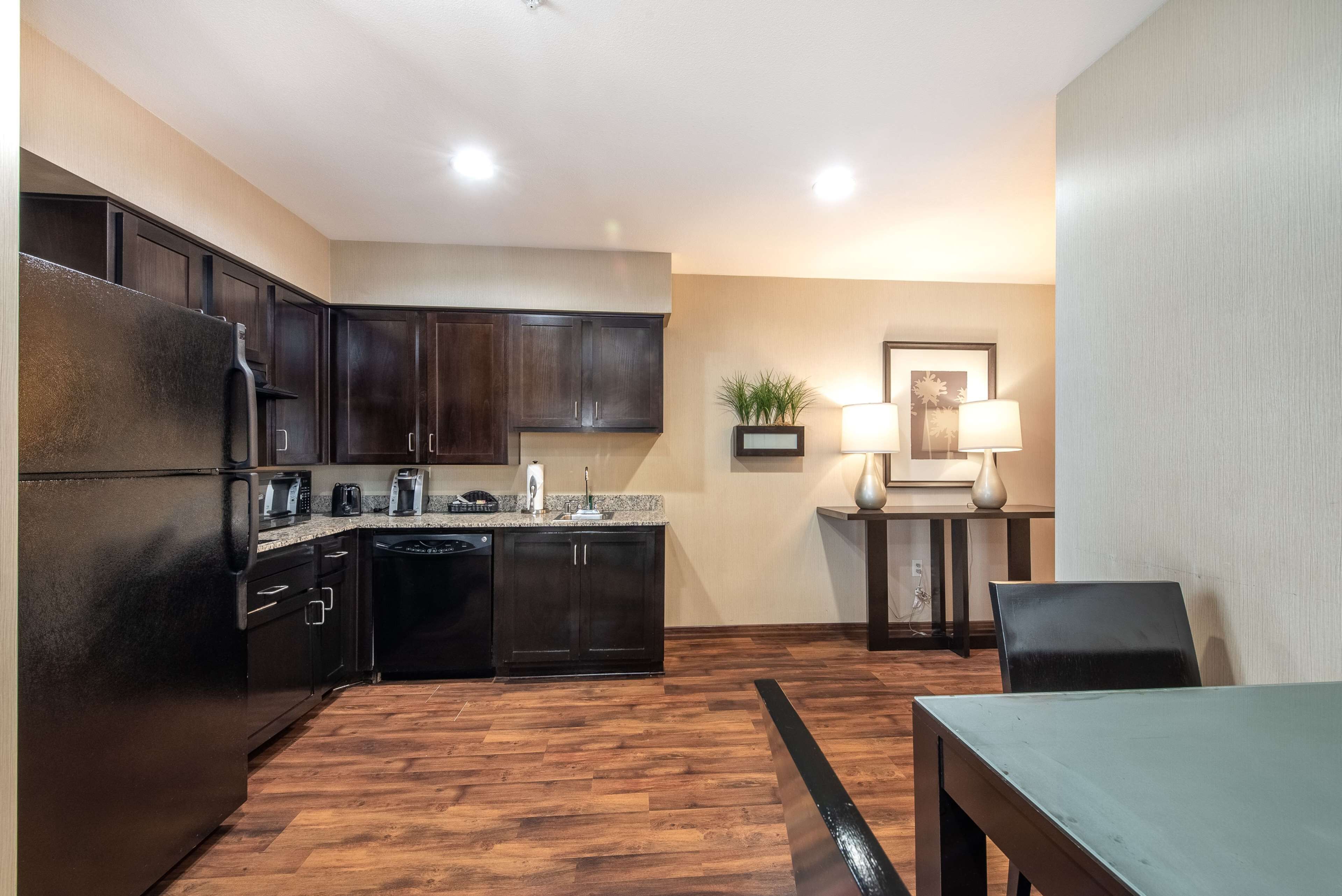 A modern kitchen with dark cabinetry, a stainless steel refrigerator, and a wooden floor.