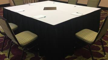 Un salón de conferencias con una gran mesa rectangular, cuatro sillas, un pequeño atril y un cuadro en la pared.