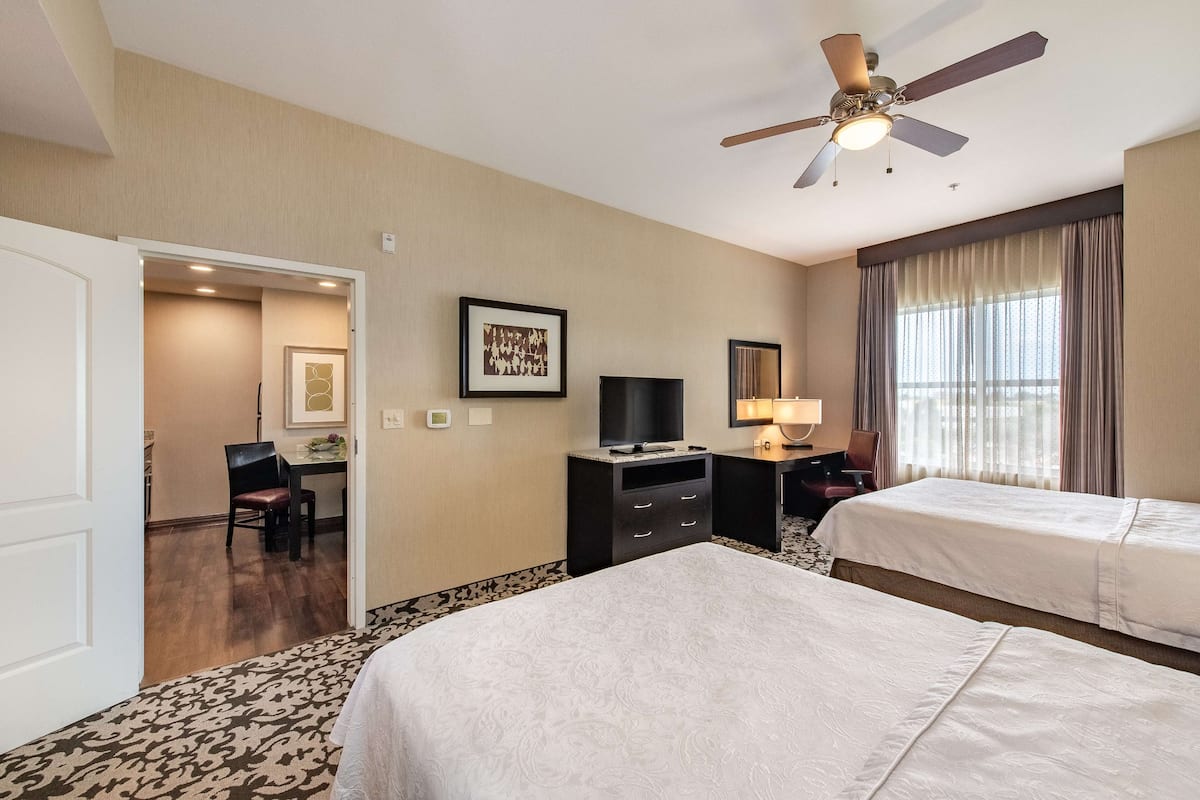 Ein Hotelzimmer mit zwei Betten, einem Schreibtisch, einem Fernseher und einem Deckenventilator.