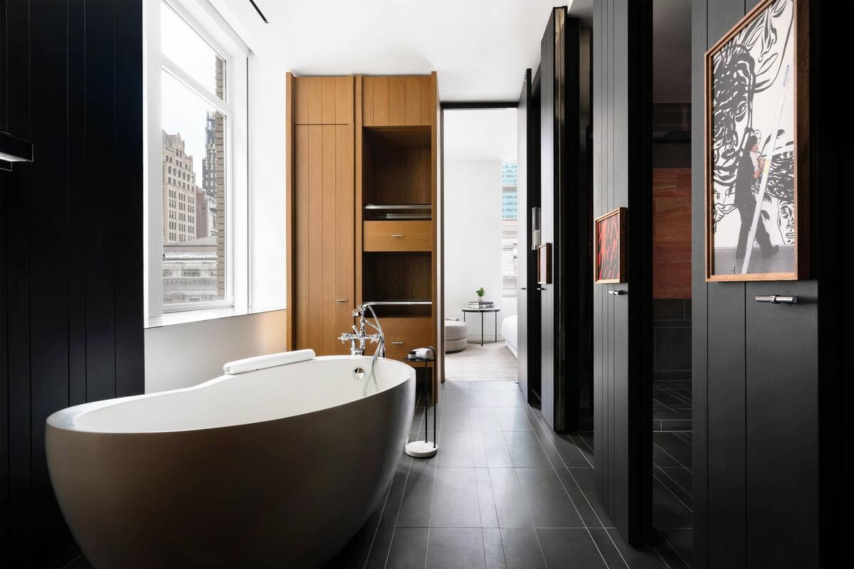 Un bany modern amb una banyera autònoma, mobles de fusta i vistes a la ciutat a través d'una finestra gran.