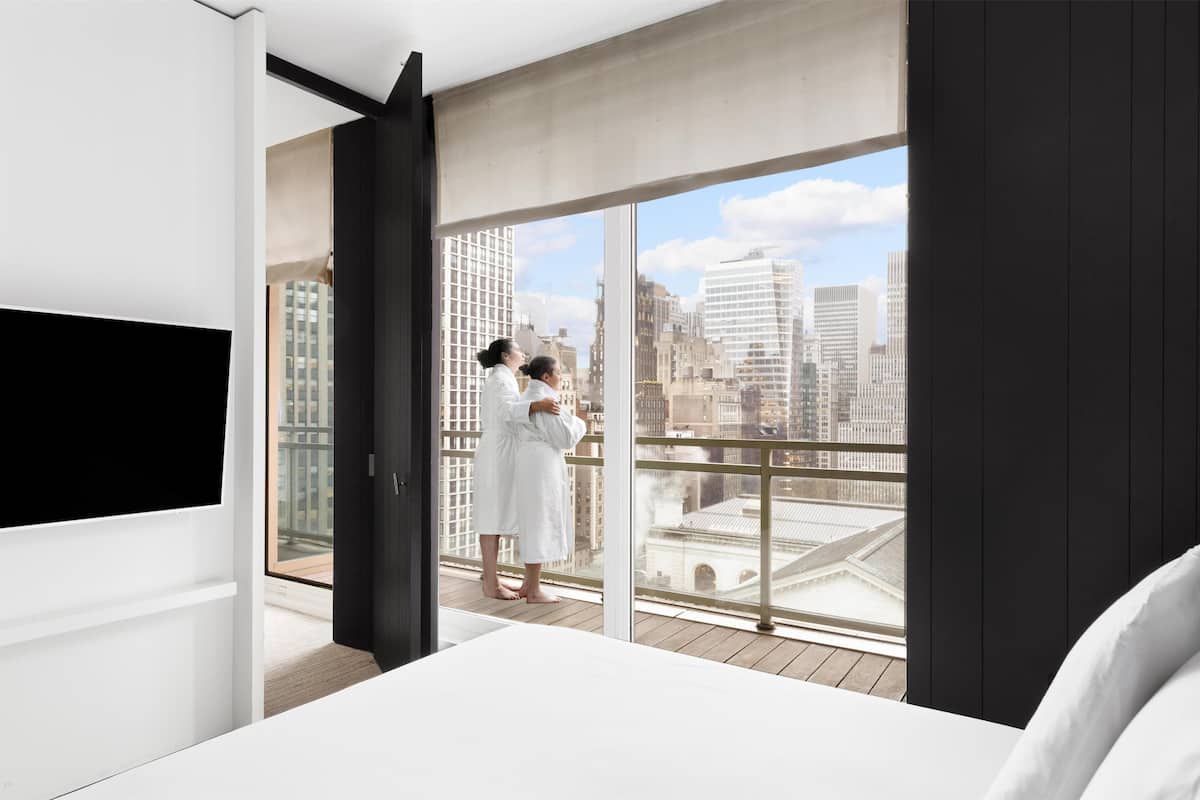 Habitació d'hotel moderna amb una finestra gran, un llit i una televisió.