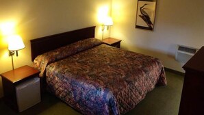 A hotel room with a bed, two bedside lamps, a nightstand, a small refrigerator, a wall-mounted air conditioner, and a framed picture on the wall. - Humboldt Redwoods Inn (Garberville)