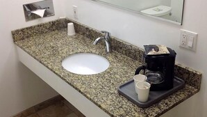 A bathroom with a granite countertop sink, a mirror, a towel rack, and a coffee maker. - Humboldt Redwoods Inn (Garberville)