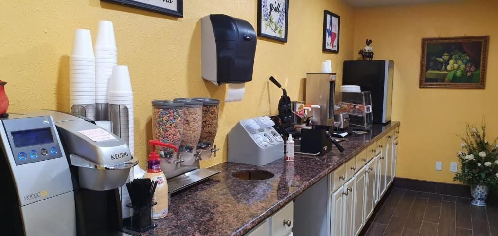 A coffee station with a Keurig machine, paper cups, a coffee dispenser, and a coffee maker.