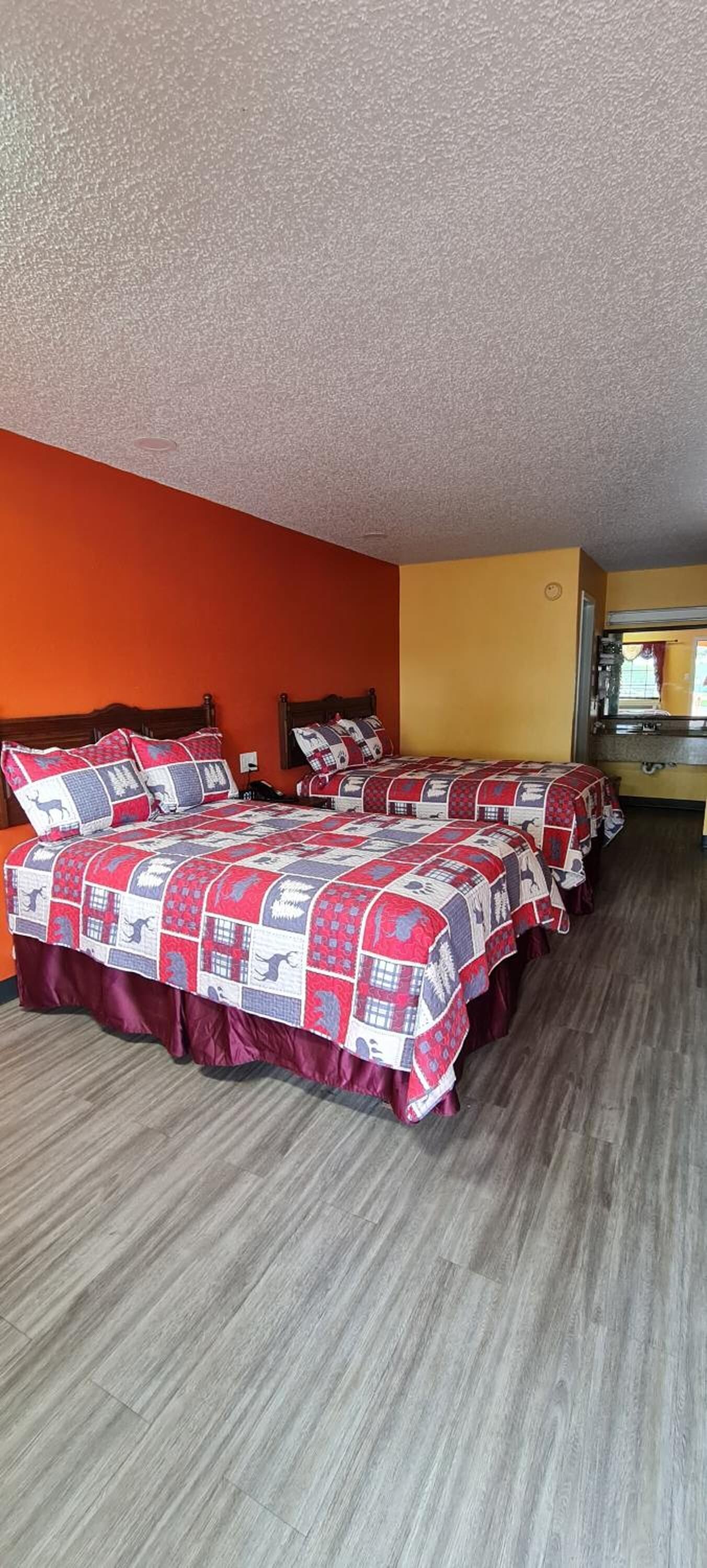A hotel room with two beds, each with a red and white quilt. The room has orange walls and a wooden floor.