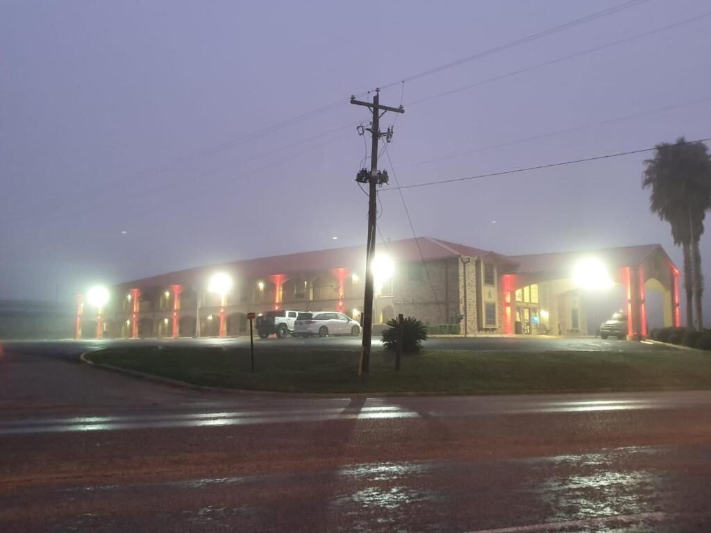 Un bâtiment dont la façade est illuminée de rouge, avec un espace de stationnement bien visible et un poteau électrique au premier plan.