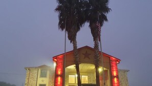 A building with a star emblem, a red-lit entrance, and palm trees. - Chaparral Motel (Hallettsville)