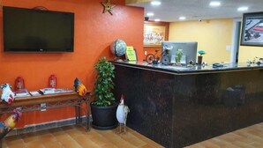 A reception area with a black reception desk, a television mounted on the wall, and a potted plant. - Chaparral Motel (Hallettsville)