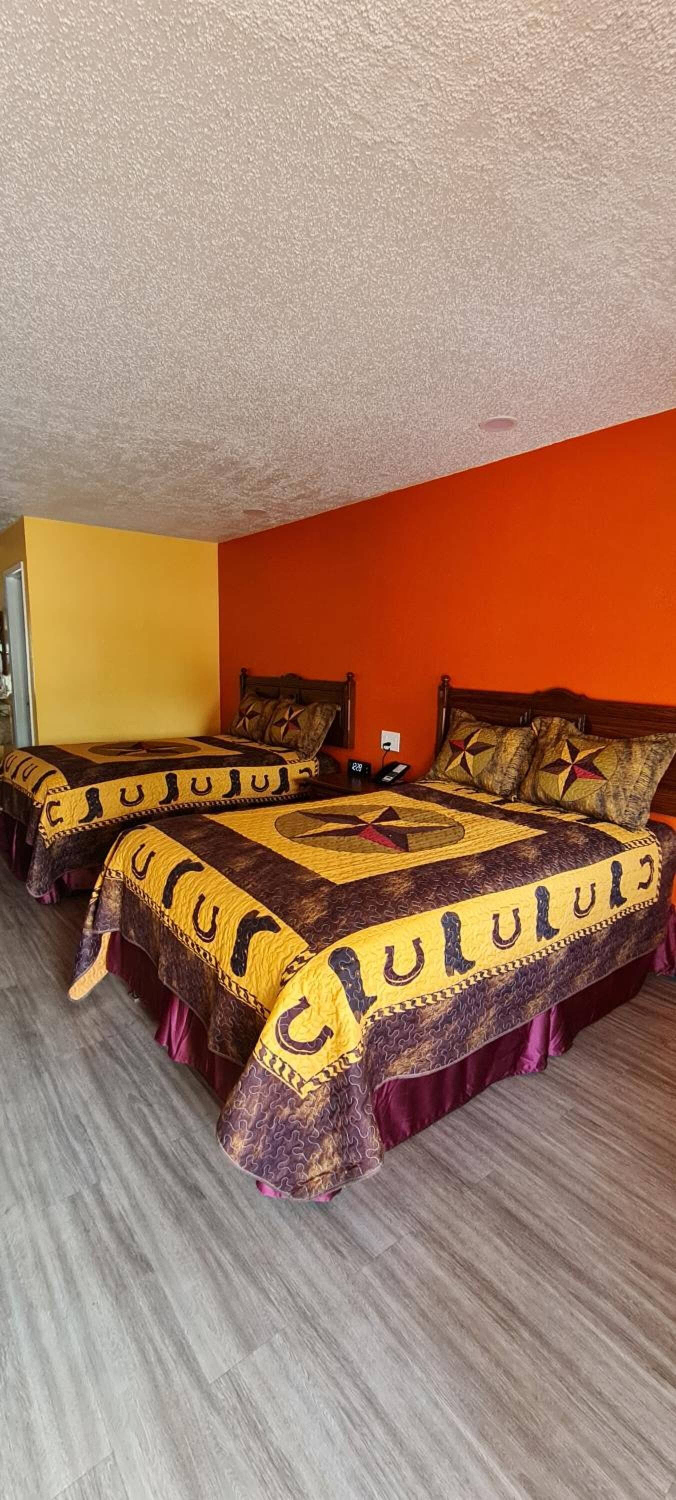 A hotel room with two beds, each covered with a patterned bedspread and pillows, and a wooden headboard.