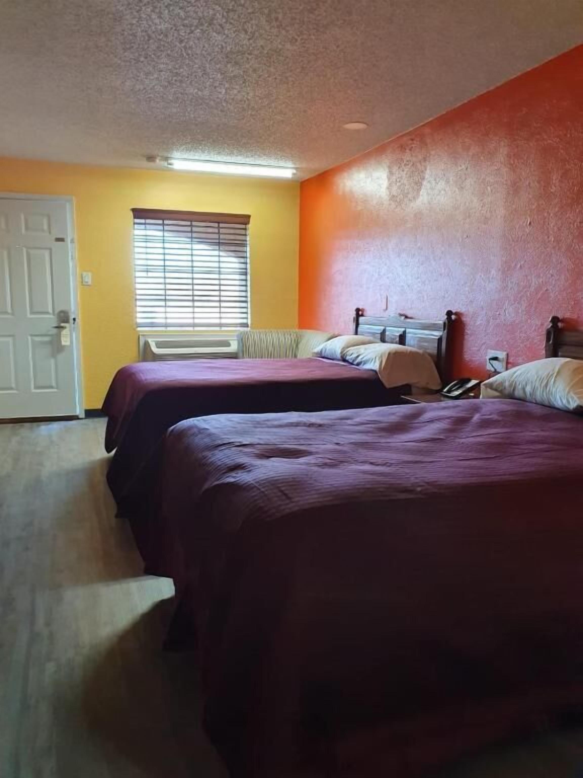 A room with two beds, a door, and a window with blinds.