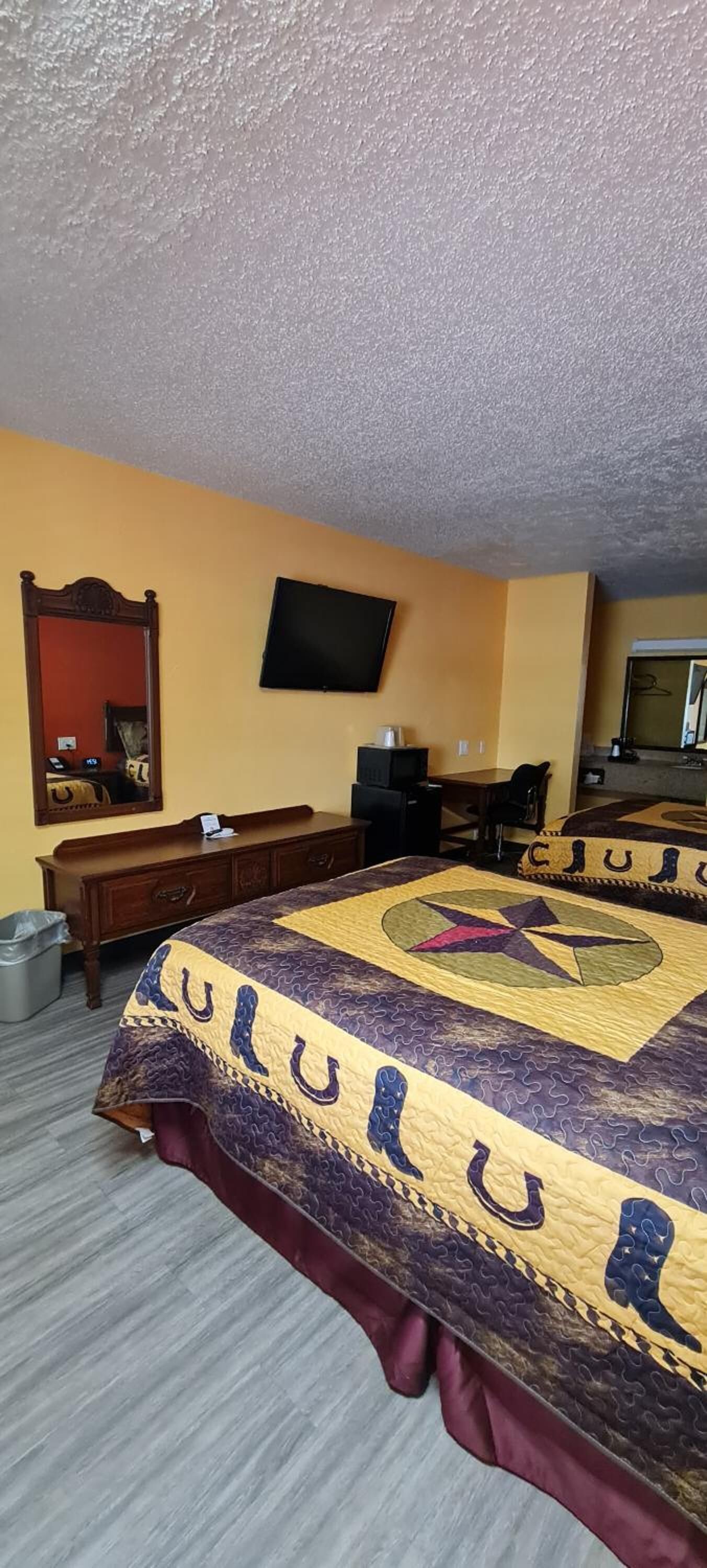 A hotel room with a large bed, a flat-screen TV, a wooden dresser, and a mirror.