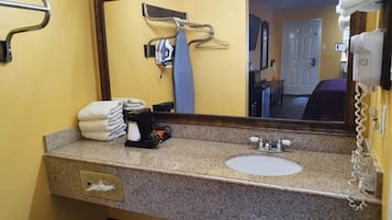 Un baño de hotel con encimera de granito, un lavamanos, un espejo, un perchero para toallas y un teléfono.