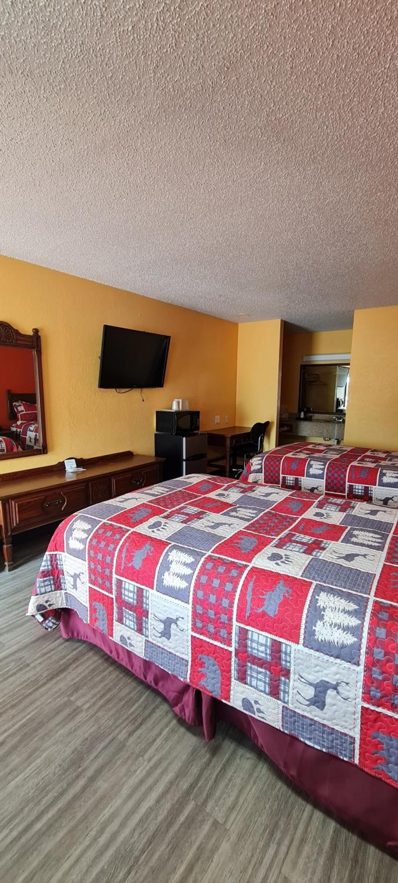 Une chambre d’hôtel avec deux lits, un téléviseur à écran plat, une commode en bois et un four à micro-ondes.