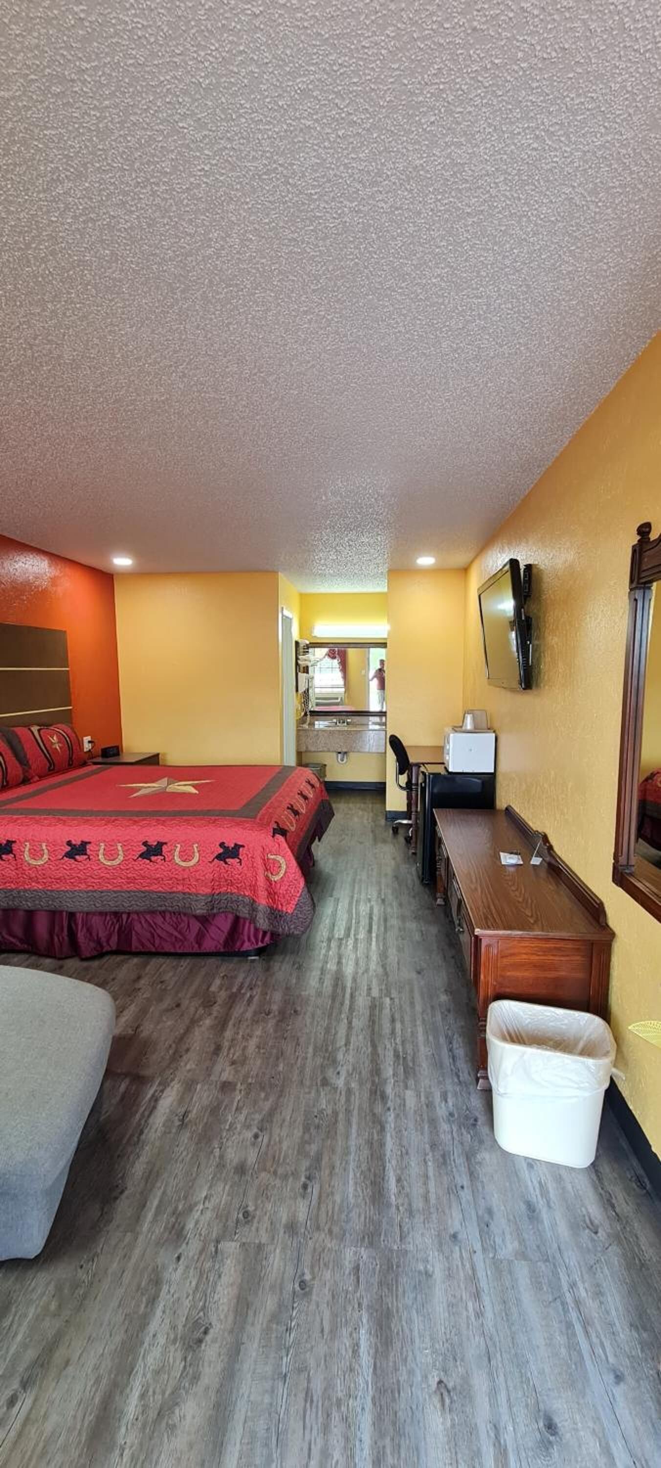 A hotel room with two beds, a desk, a chair, a TV, and a trash bin.