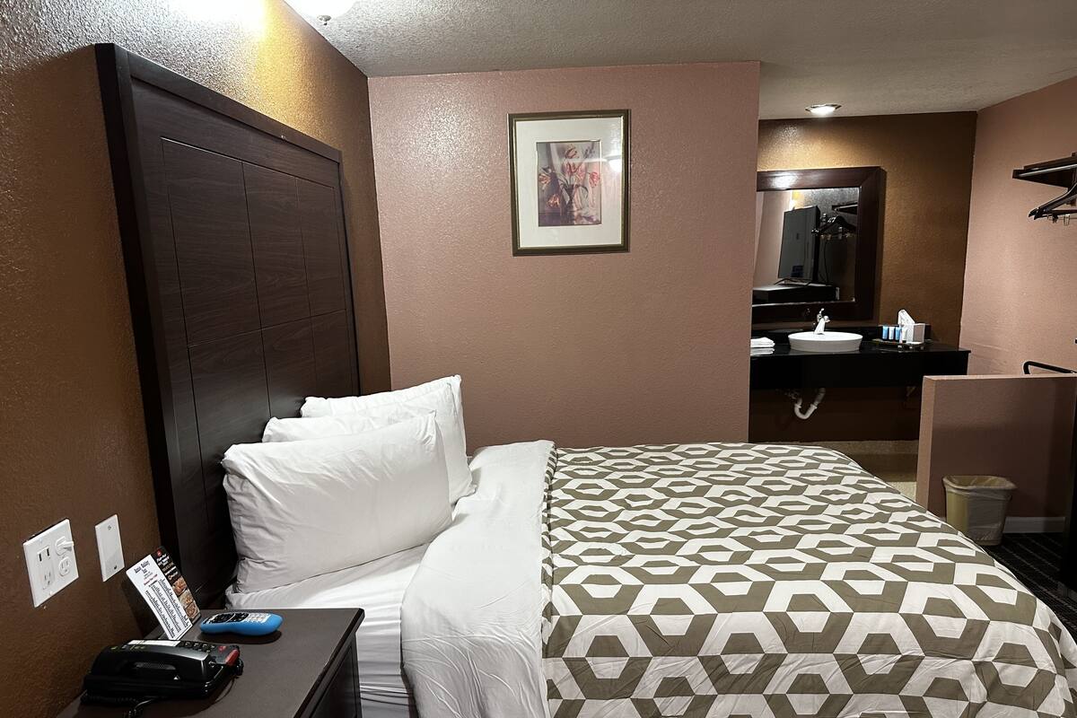 A hotel room with a bed, a desk with a telephone and papers, a mirror, and a sink in the bathroom.