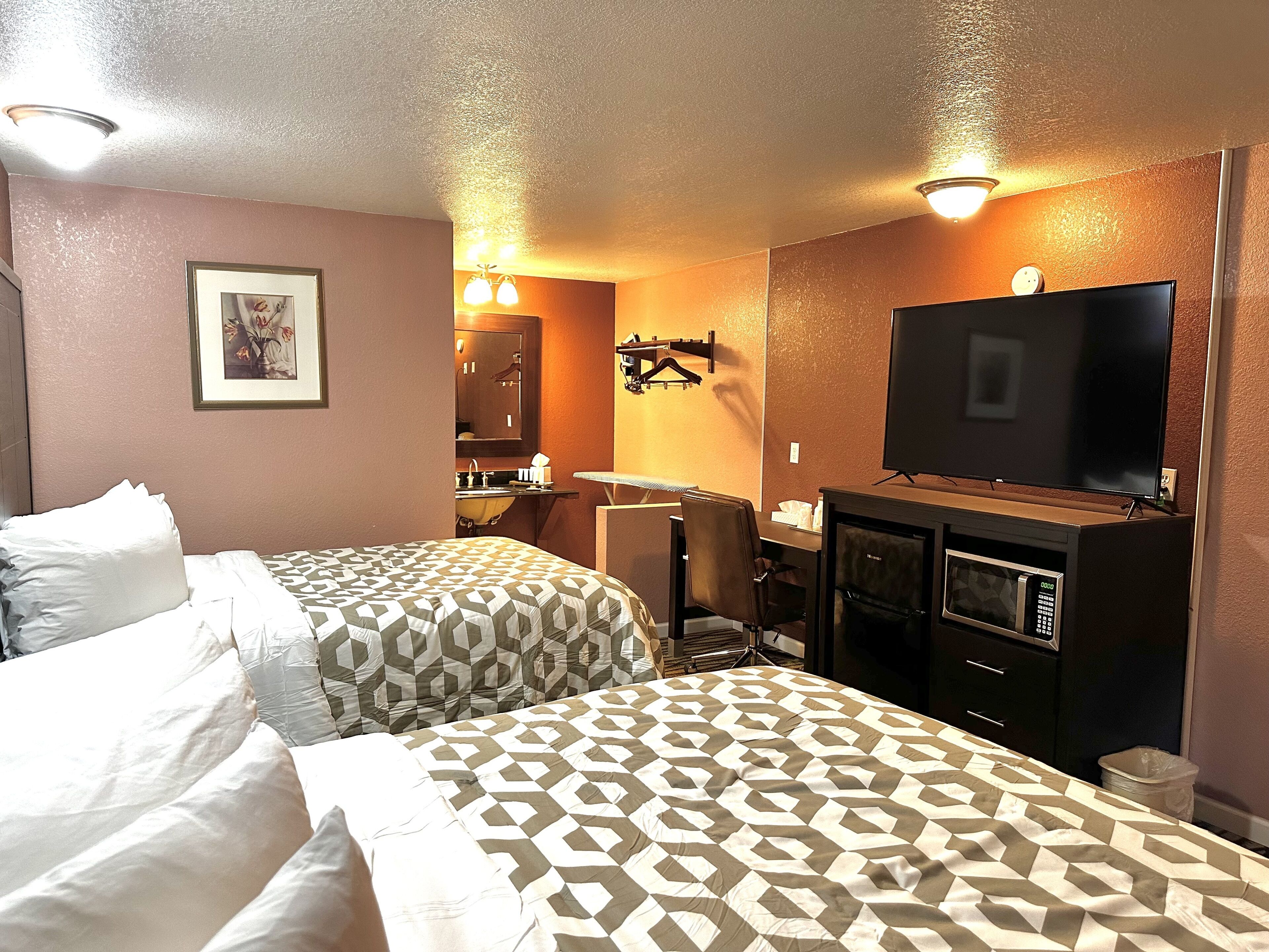 Habitación de hotel con dos camas, televisión, microondas y baño visible a través de una puerta abierta.