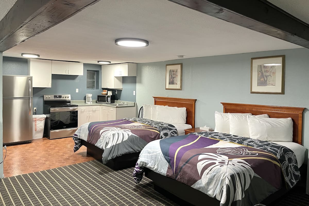 A hotel room with two beds, a kitchenette, and a bathroom.