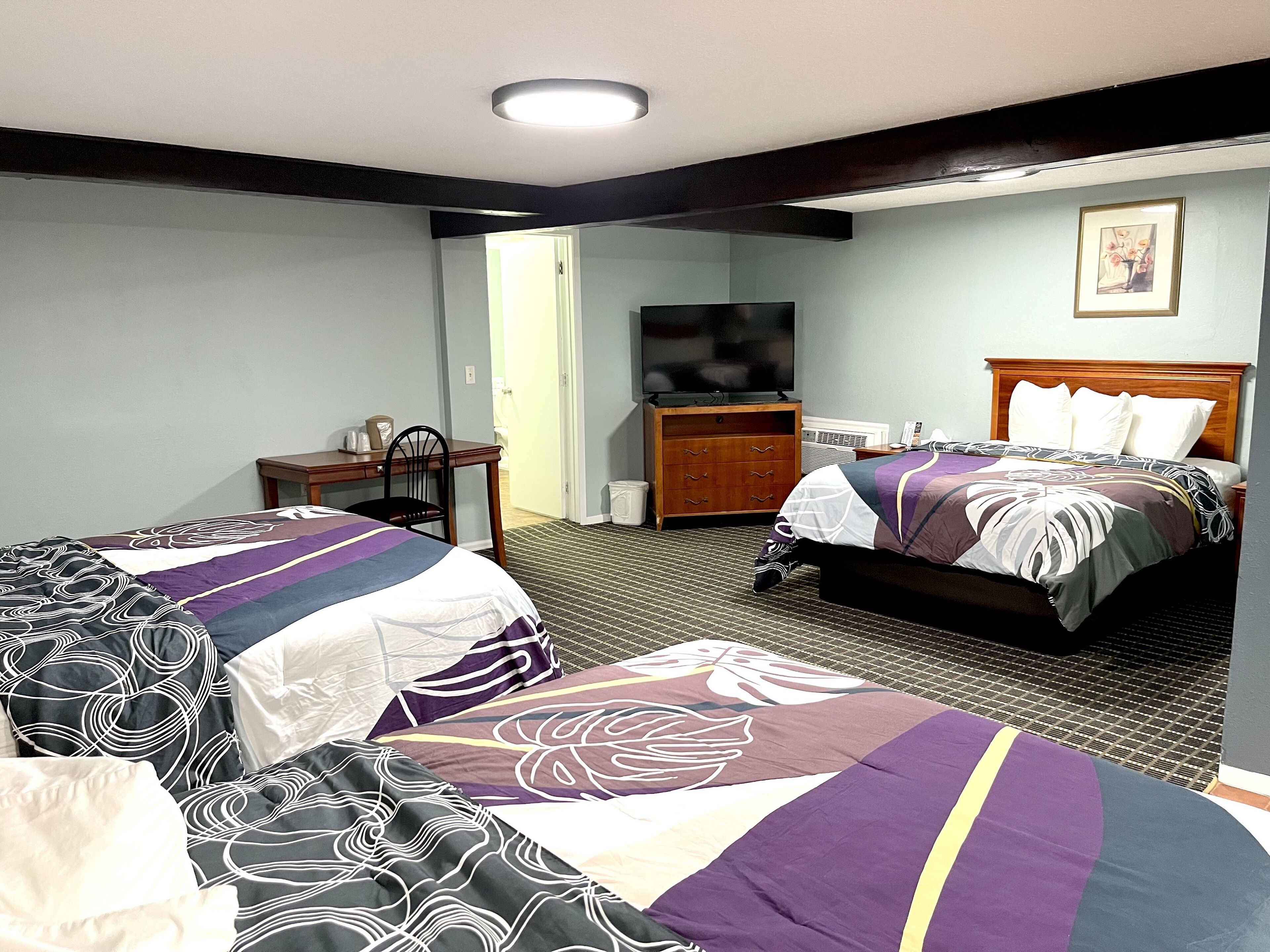 A hotel room with two beds, a desk, a chair, a television, and a framed picture on the wall.