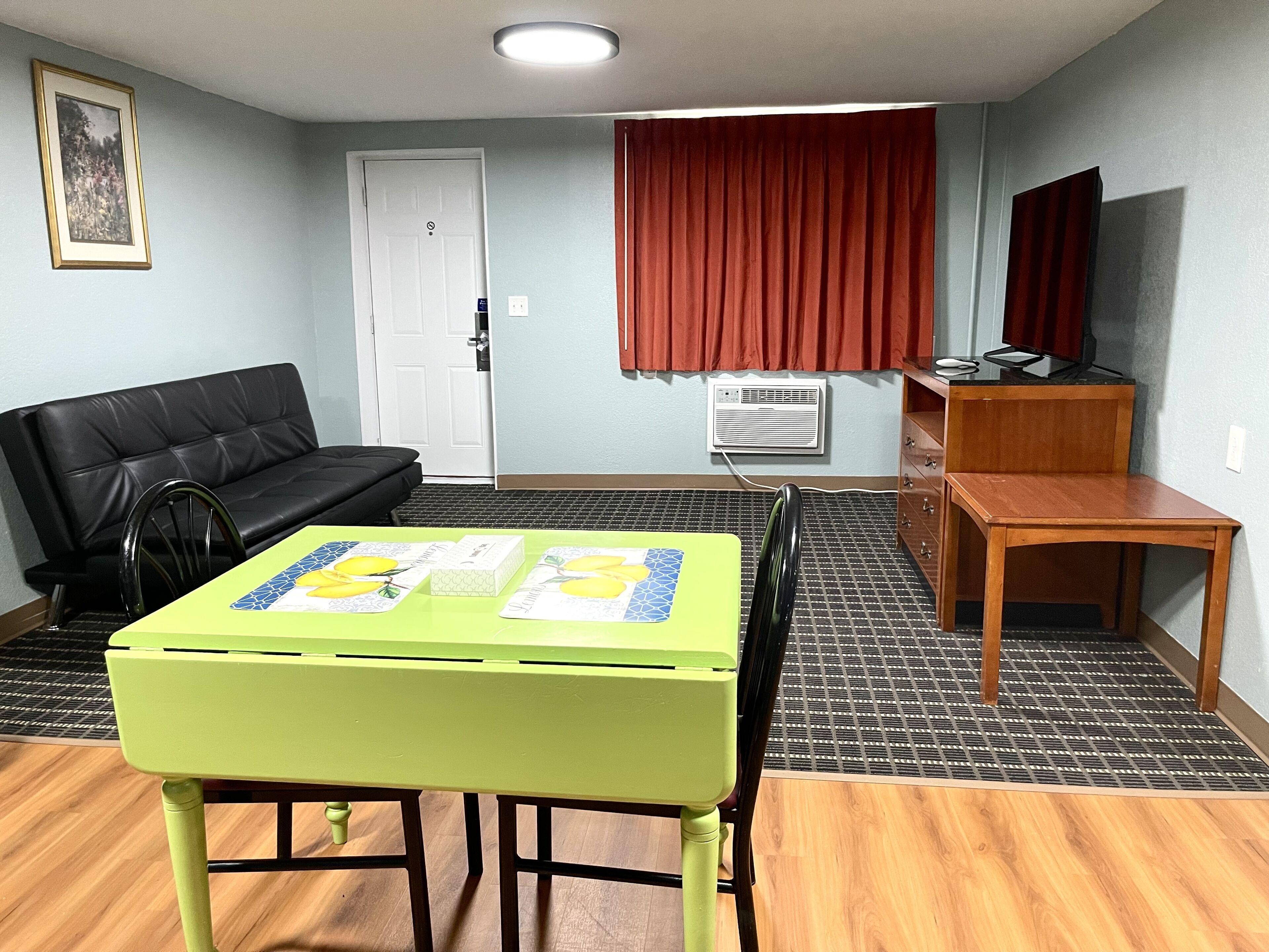 A room with a green table, a black sofa, a wooden cabinet, and a red curtain.