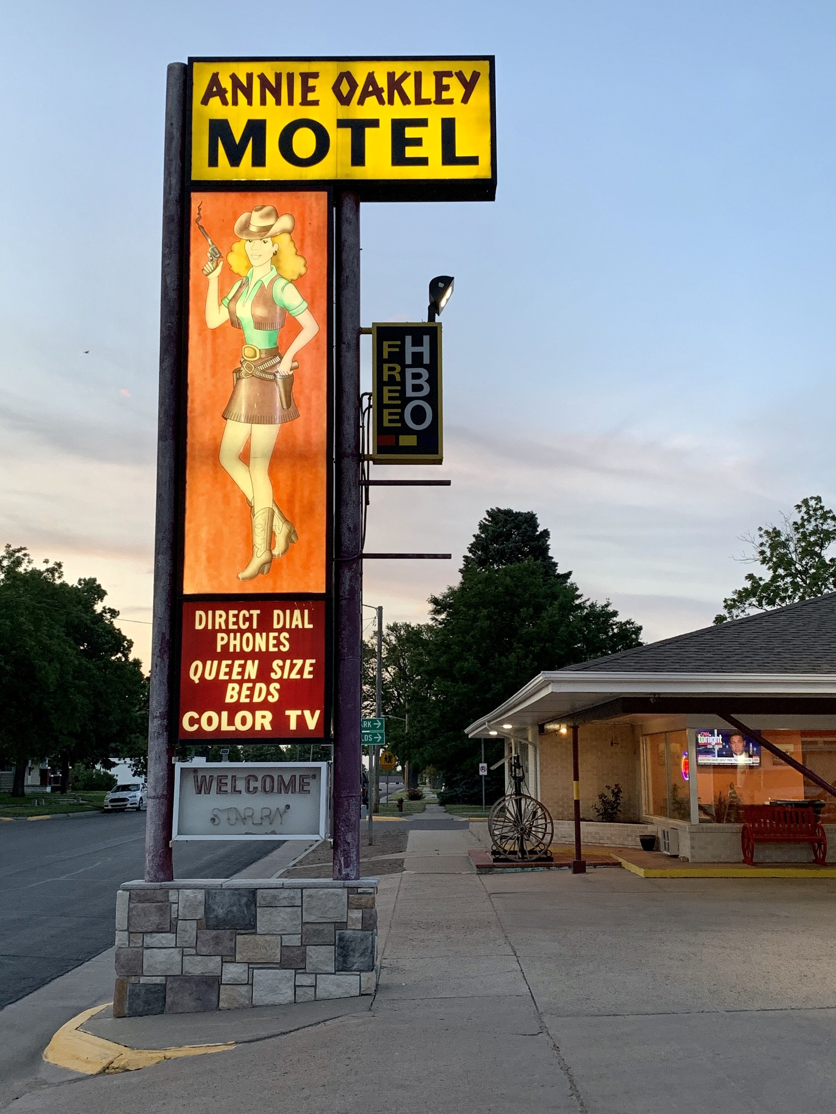 A motel sign with a woman illustration, direct dial phones, queen size beds, and color TV.