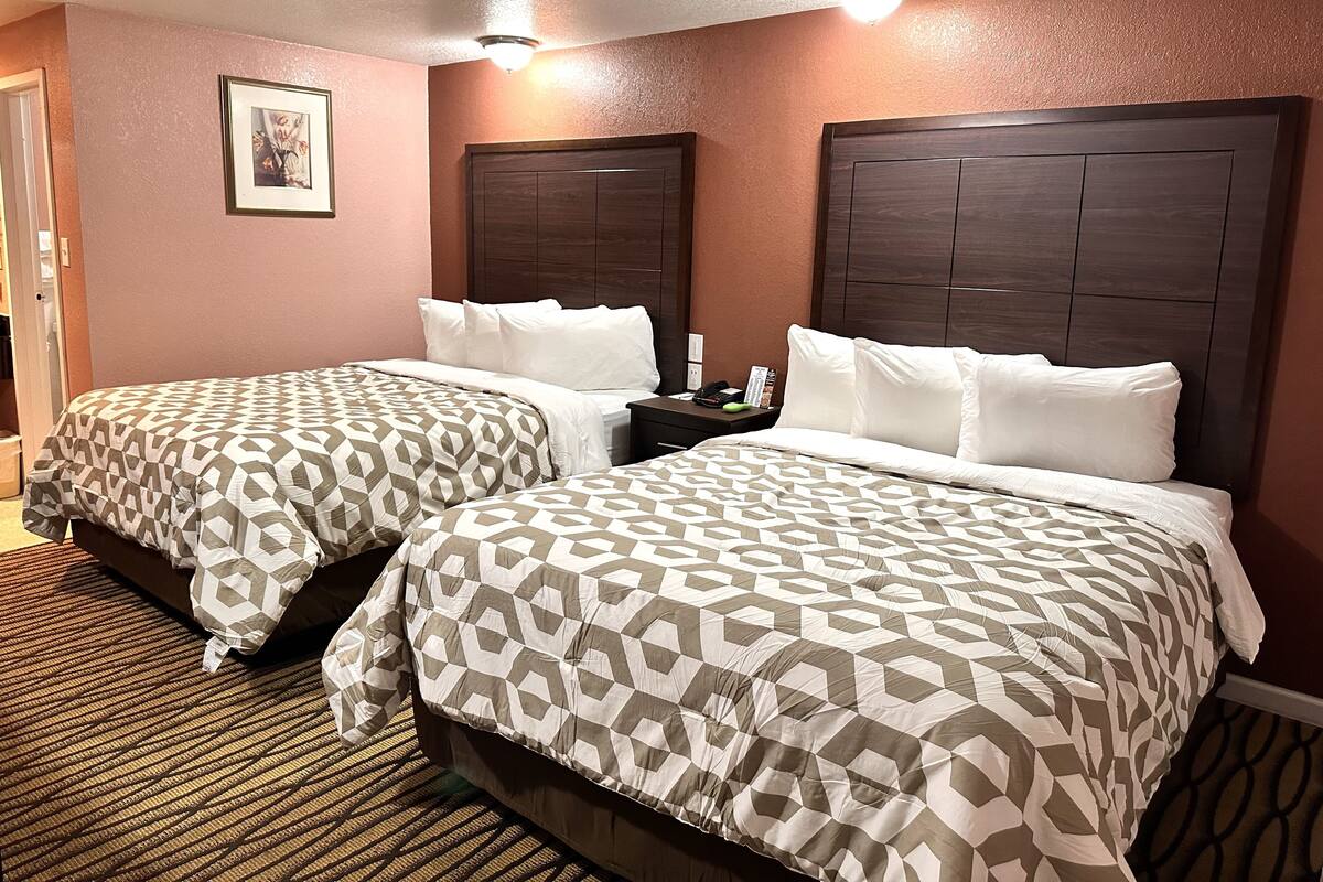 A hotel room with two beds, each with a patterned bedspread, a nightstand with a phone and a book, and a framed picture on the wall.
