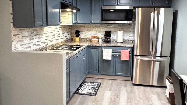 A modern kitchen with grey cabinets, stainless steel appliances, and a patterned backsplash. - Annie Oakley Motel Oakley (Oakley)