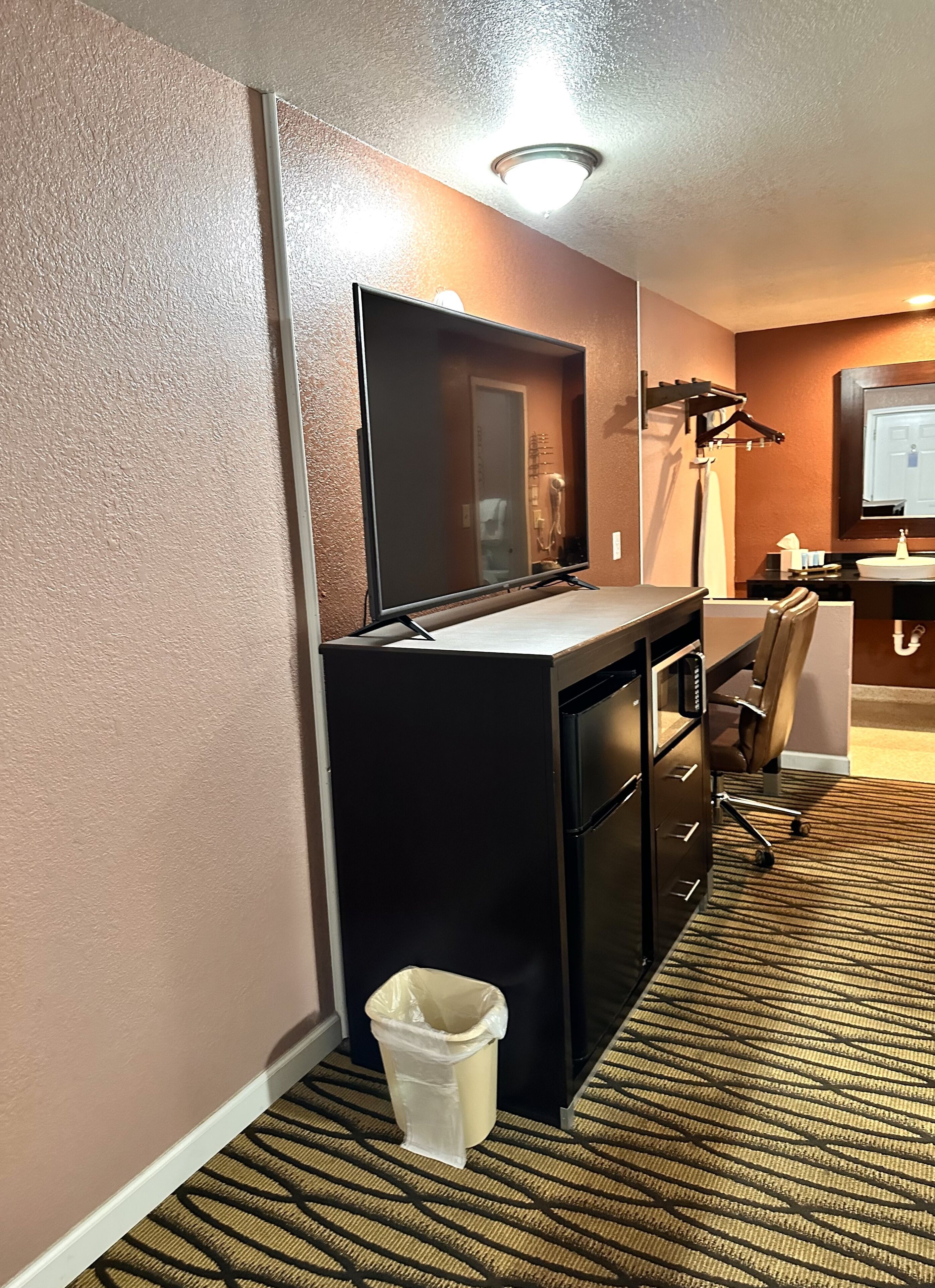 Habitación de hotel con escritorio, silla y un cubo de basura.