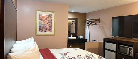 A hotel room with a bed, a TV, a desk with a microwave, a sink, and a mirror.