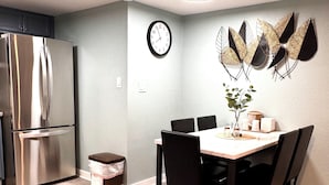 A modern kitchen with a stainless steel refrigerator, a dining table with chairs, a wall clock, and decorative wall art. - Annie Oakley Motel Oakley (Oakley)
