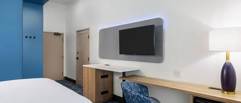 A hotel room with a bed, a desk with a chair, a flat-screen TV, a lamp, and a microwave.