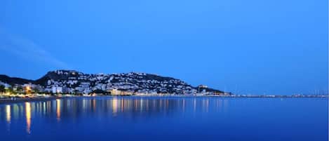 A coastal town at dusk with buildings reflecting on calm water.