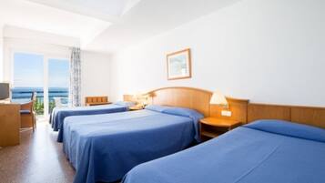 Habitación de hotel con tres camas, cabecera de madera, mesita de noche con lámpara y un cuadro enmarcado en la pared.