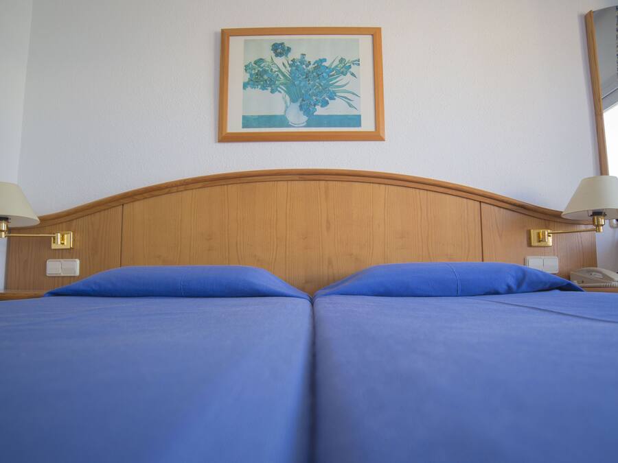 A double bed with blue bedding, two bedside lamps, a framed artwork on the wall, and a nightstand with a telephone.