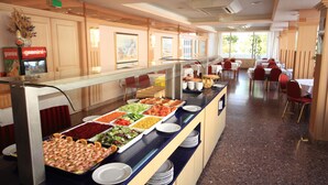Un bufé amb diverses opcions gastronòmiques i una zona de seients amb cadires vermelles i taules blanques.