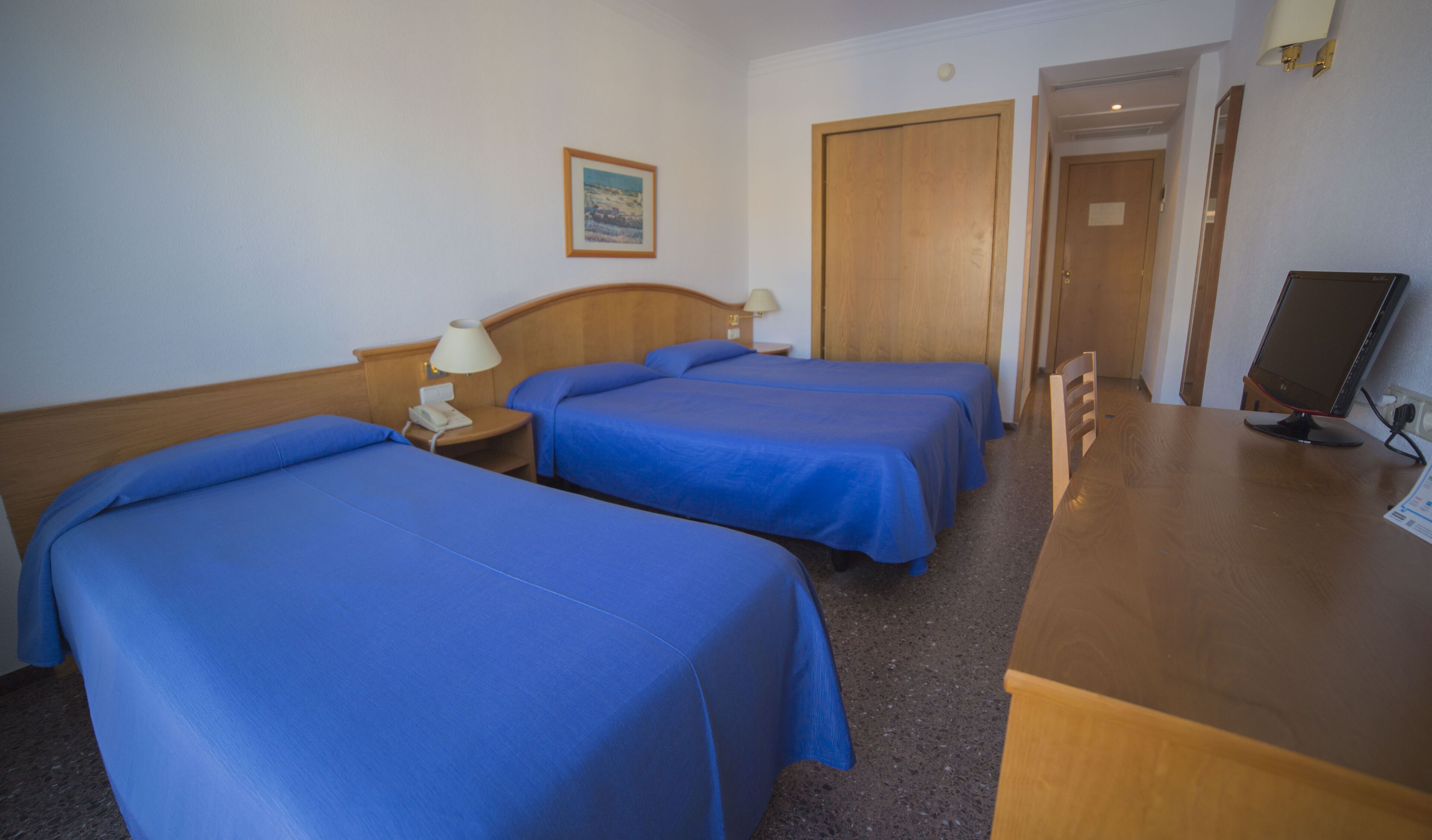 A hotel room with two beds, a desk, a computer, and a door leading to another room.
