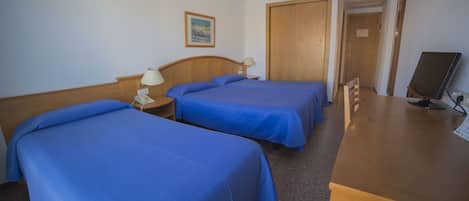 A hotel room with two beds, a desk, a computer, and a door leading to another room.