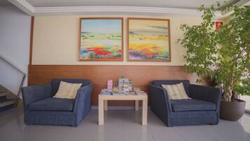 Un hall d’entrée avec deux fauteuils bleus, une table en bois sur laquelle sont posés des magazines, et deux tableaux représentant des paysages accrochés au mur.