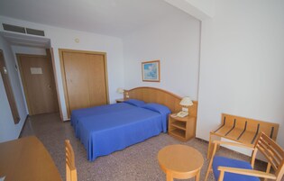 A hotel room with a bed, a desk, a chair, a nightstand, and a painting on the wall.