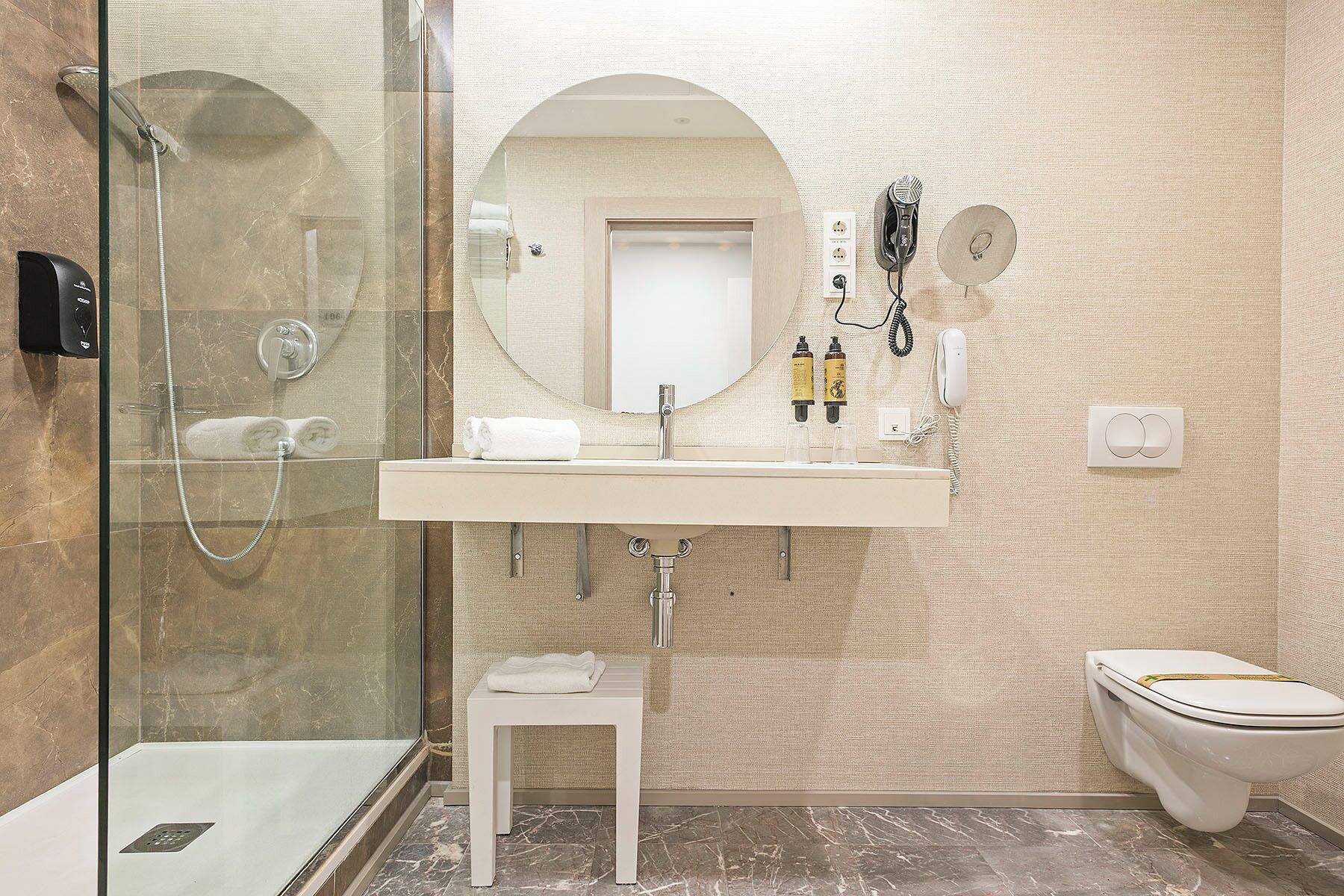 A modern bathroom with a glass-enclosed shower, a white sink with a mirror above it, and a toilet.