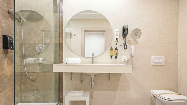A modern bathroom with a glass-enclosed shower, a white sink with a mirror above it, and a toilet. - Cullera Holiday Hotel (Cullera)