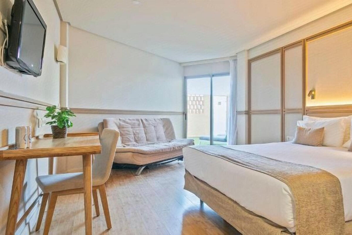 A hotel room with a bed, a desk, a chair, a sofa, and a television.