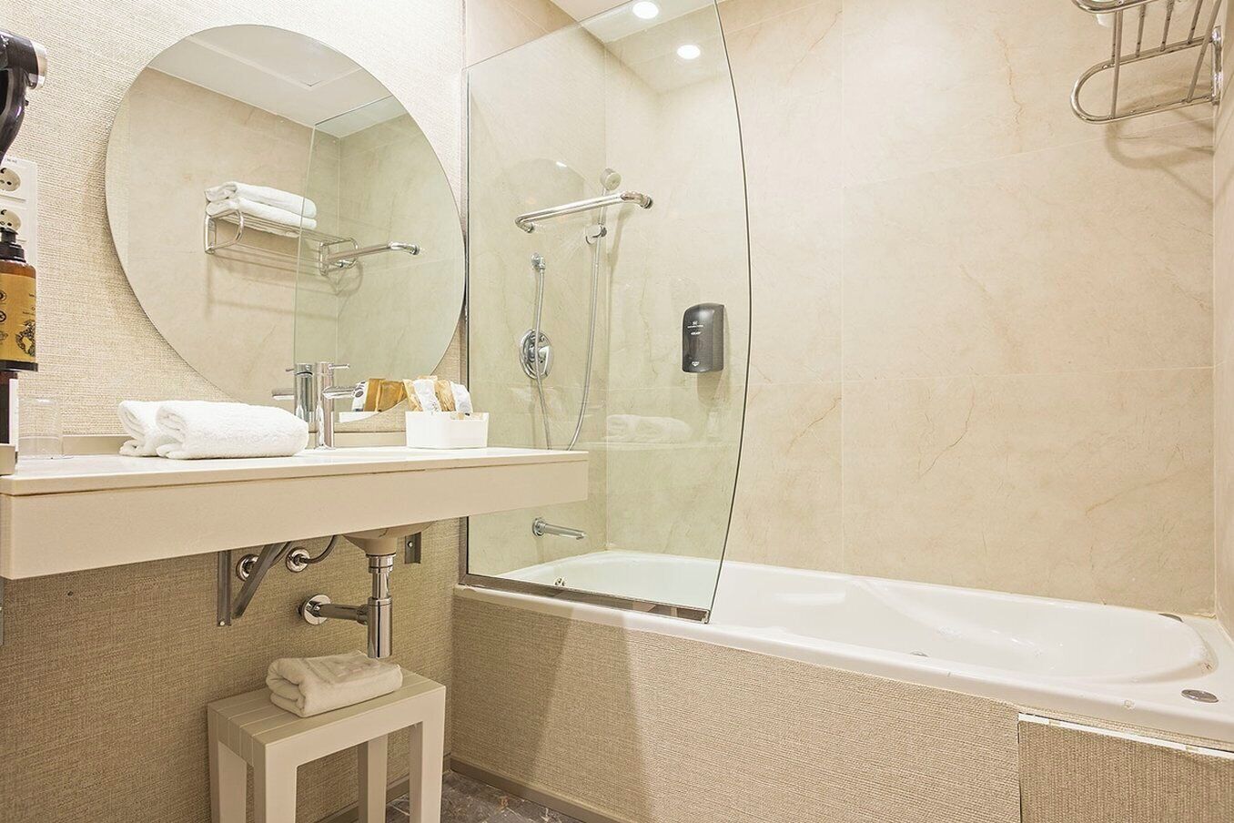 A bathroom with a bathtub, a shower, a round mirror, and a vanity with a towel.