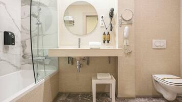 Une salle de bain avec une douche à parois de verre, un lavabo blanc avec un miroir, des toilettes et un petit tabouret.