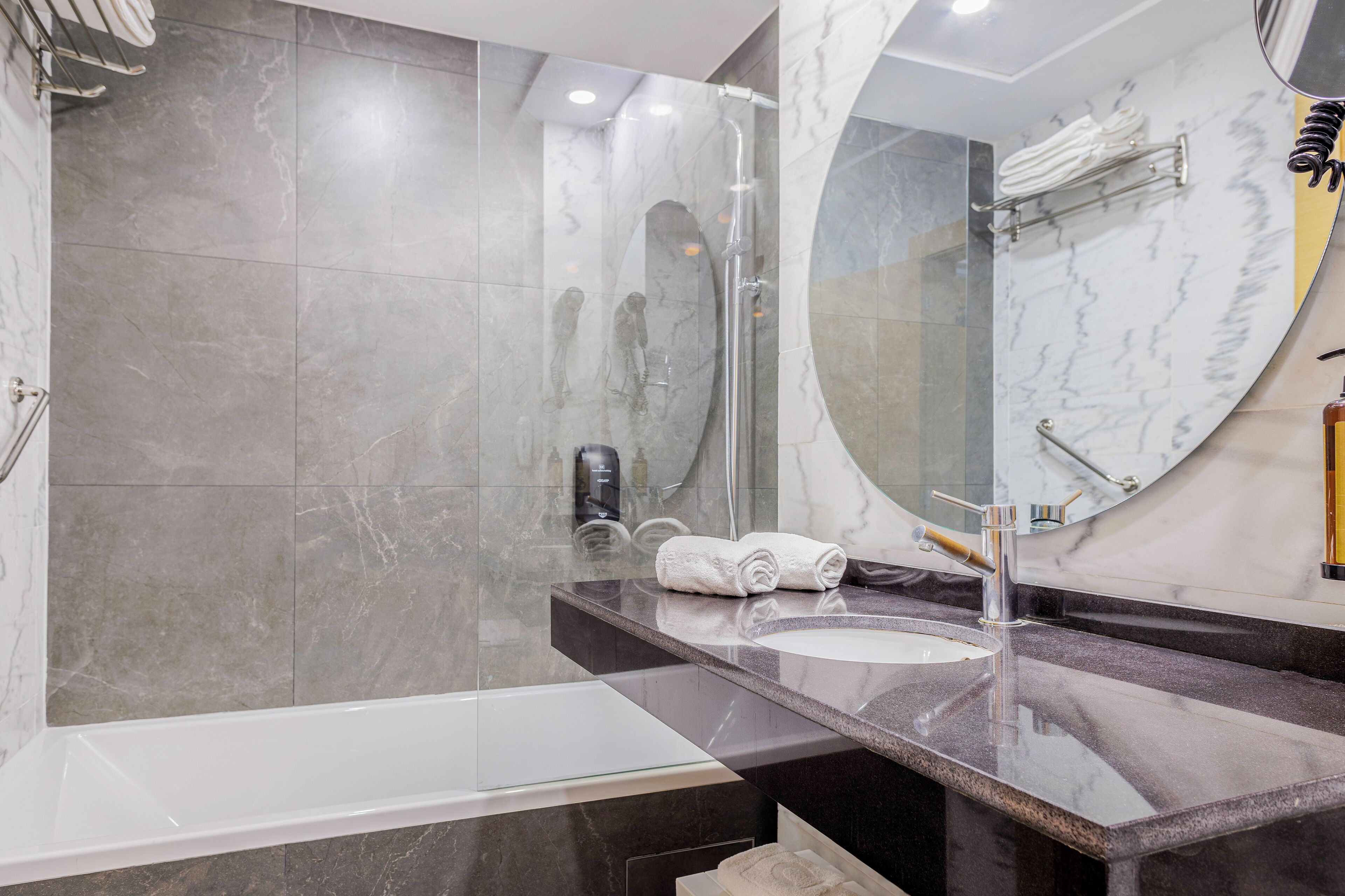 Un baño moderno con ducha envuelta en vidrio, un espejo grande y pared revestida de mármol.