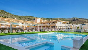A swimming pool with lounge chairs and umbrellas, surrounded by buildings with balconies and a hilly backdrop. - Cullera Holiday Hotel (Cullera)