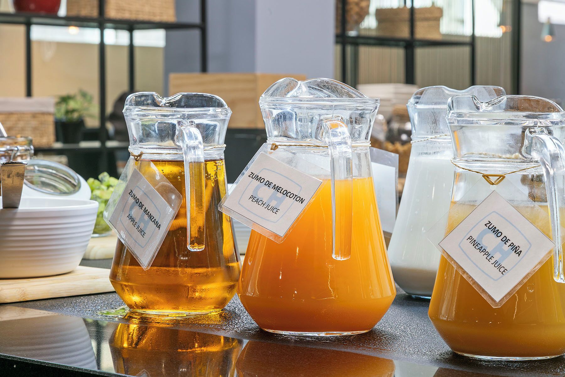 Cuatro jarras de vidrio con etiquetas que identifican diferentes zumos de frutas.
