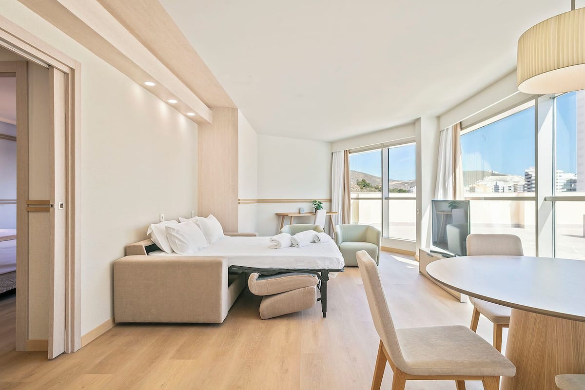 A modern hotel room with a bed, seating area, and large windows offering a view.