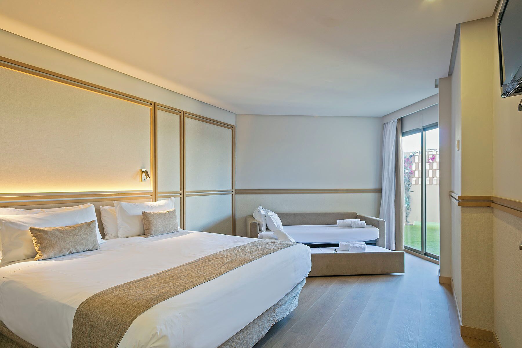 A hotel room with a large bed, a smaller bed, a sofa, and a large window.